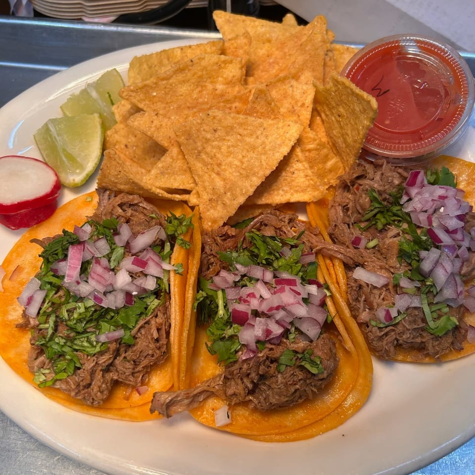 Three shredded meat tacos with onion and cilantro, tortilla chips, lime and salsa.