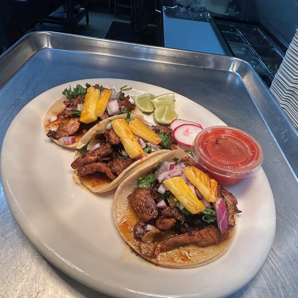 Three tacos topped with pineapple, onion and cilantro, served with lime and salsa.